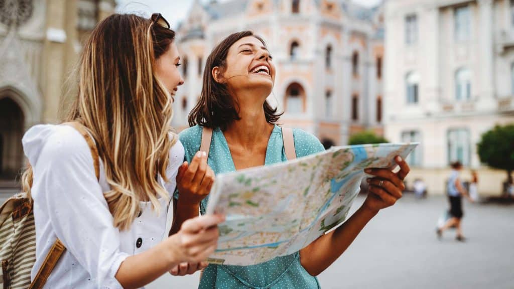 Two young women holding map and exploring city