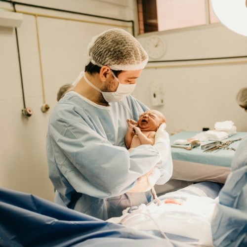 Doctor holding new born baby - bed side