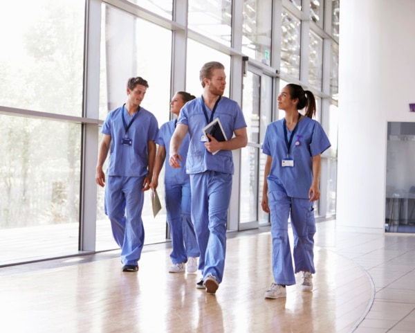 Four healthcare workers in scrubs walking in corridor
